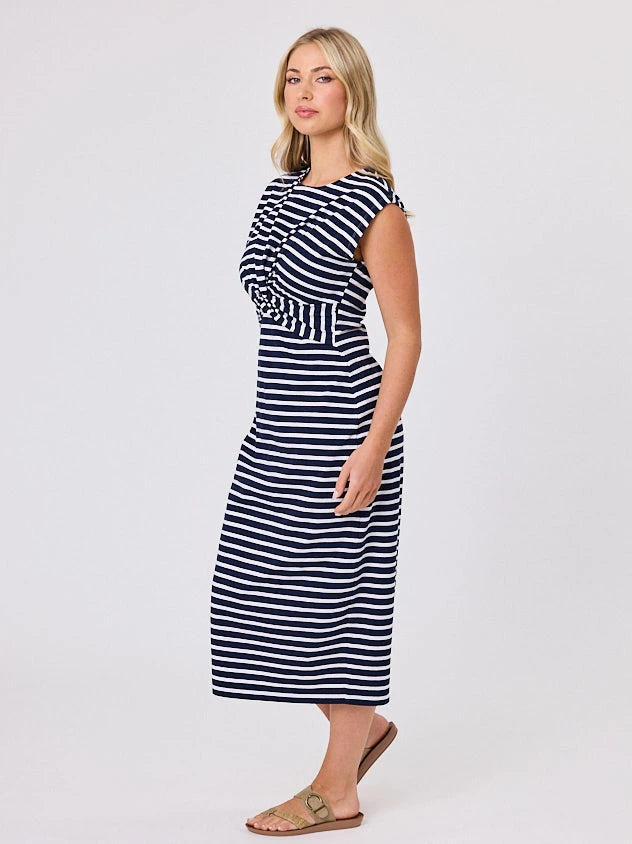 Woman wearing a coastal living inspired navy blue striped cotton dress by Navy & Co, standing front-facing in natural light