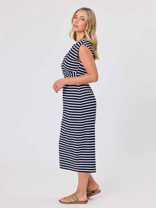Woman wearing a coastal living inspired navy blue striped cotton dress by Navy & Co, standing front-facing in natural light