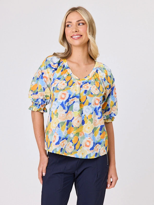 Woman wearing a vibrant colourful lemon yellow floral pattern cotton top by Navy & Co fashion brand, standing front-facing in natural light