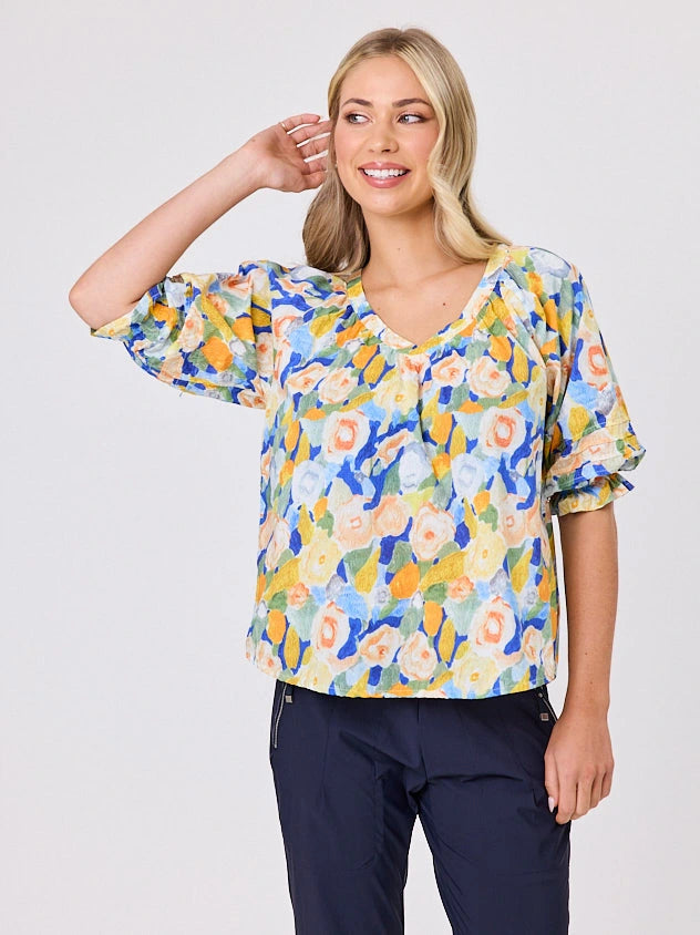 Woman wearing a vibrant colourful lemon yellow floral pattern cotton top by Navy & Co fashion brand, standing front-facing in natural light