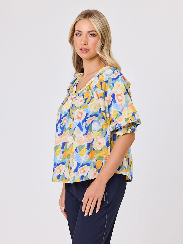 Woman wearing a vibrant colourful lemon yellow floral pattern cotton top by Navy & Co fashion brand, standing front-facing in natural light