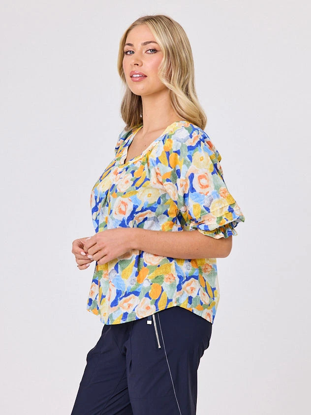 Woman wearing a vibrant colourful lemon yellow floral pattern cotton top by Navy & Co fashion brand, standing front-facing in natural light
