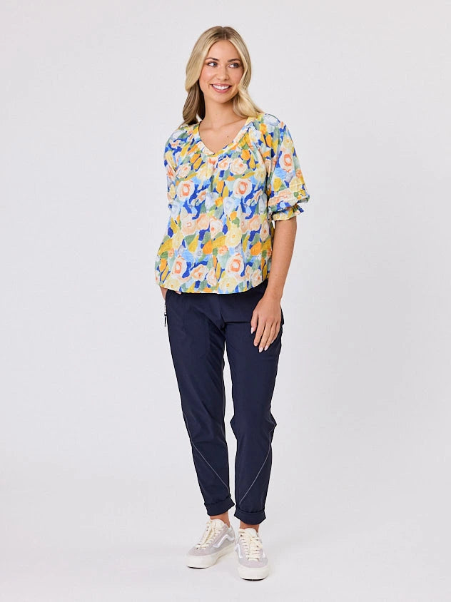 Woman wearing a vibrant colourful lemon yellow floral pattern cotton top by Navy & Co fashion brand, standing front-facing in natural light