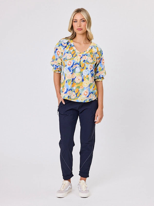 Woman wearing a vibrant colourful lemon yellow floral pattern cotton top by Navy & Co fashion brand, standing front-facing in natural light