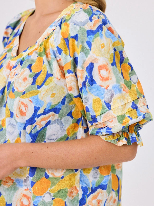 Woman wearing a vibrant colourful lemon yellow floral pattern cotton top by Navy & Co fashion brand, standing front-facing in natural light