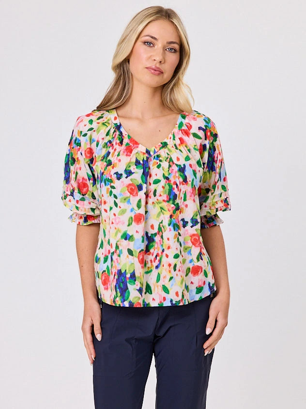 Woman wearing a vibrant colourful red floral pattern cotton top by Navy & Co fashion brand, standing front-facing in natural light