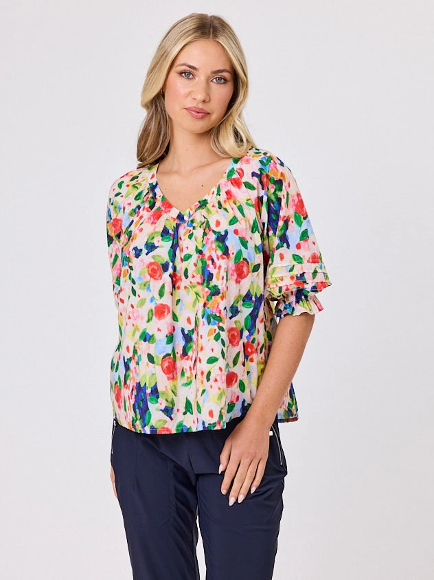 Woman wearing a vibrant colourful red floral pattern cotton top by Navy & Co fashion brand, standing front-facing in natural light