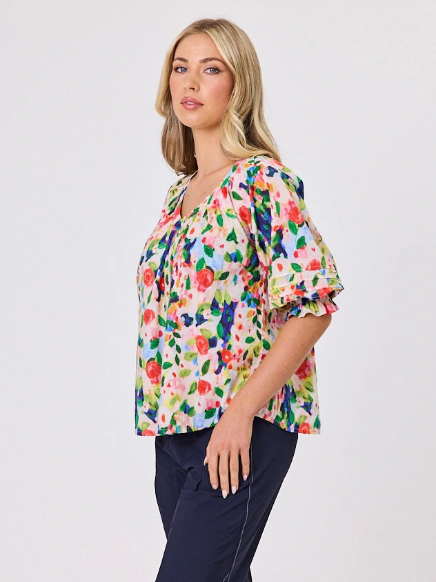 Woman wearing a vibrant colourful red floral pattern cotton top by Navy & Co fashion brand, standing front-facing in natural light