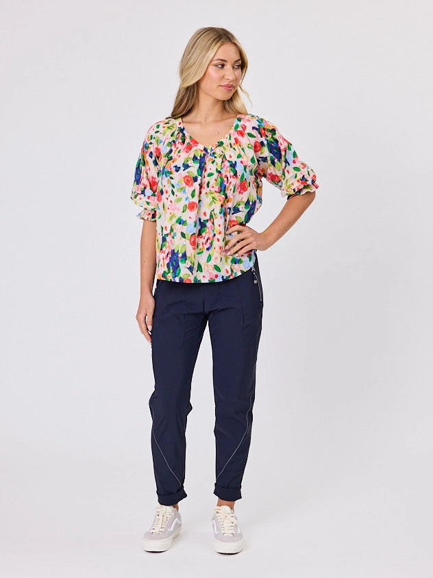 Woman wearing a vibrant colourful red floral pattern cotton top by Navy & Co fashion brand, standing front-facing in natural light
