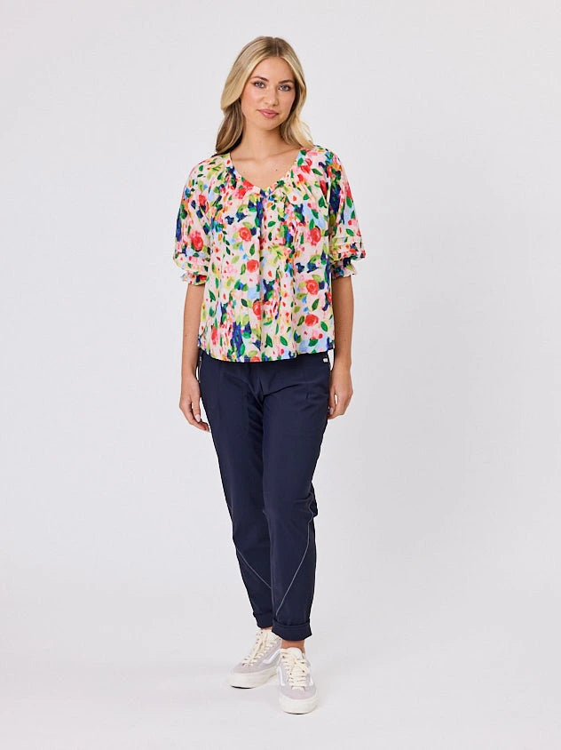 Woman wearing a vibrant colourful red floral pattern cotton top by Navy & Co fashion brand, standing front-facing in natural light