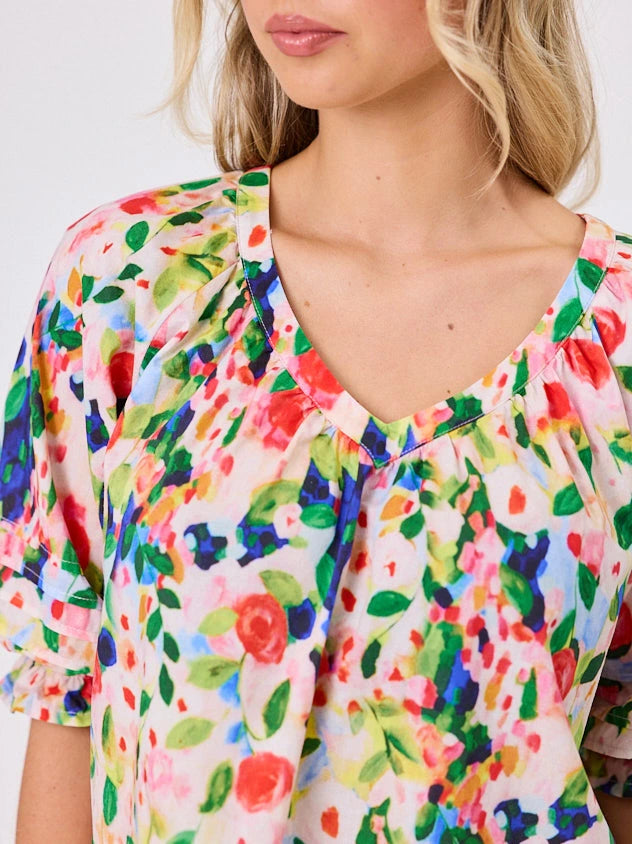 Woman wearing a vibrant colourful red floral pattern cotton top by Navy & Co fashion brand, standing front-facing in natural light