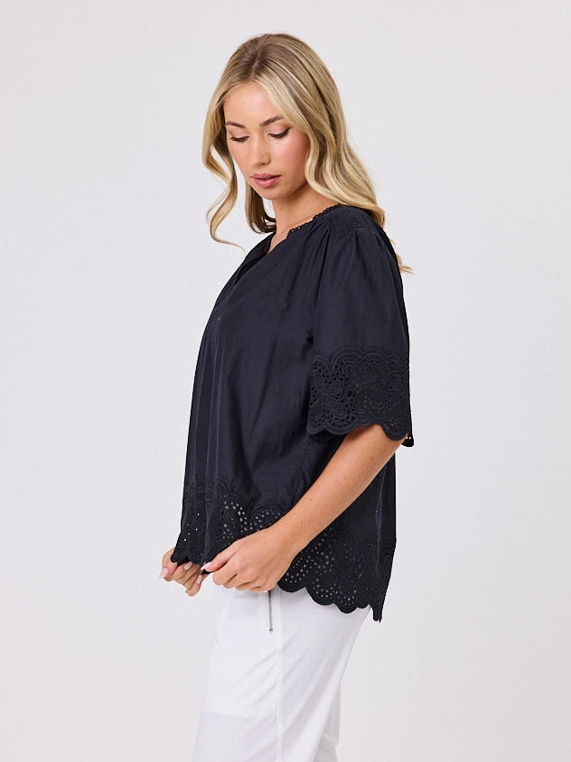 Woman wearing a black blouse with lace details standing front-on in studio light with white background. Top by Navy & Co nz fashion brand  