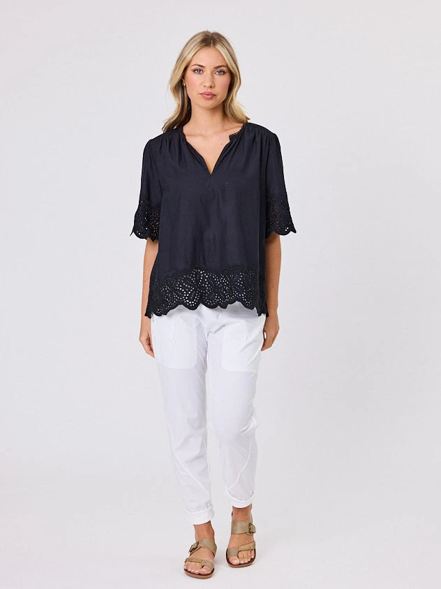 Woman wearing a black blouse with lace details standing front-on in studio light with white background. Top by Navy & Co nz fashion brand  