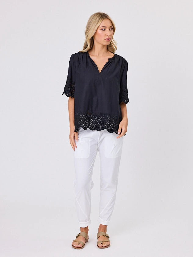 Woman wearing a black blouse with lace details standing front-on in studio light with white background. Top by Navy & Co nz fashion brand  