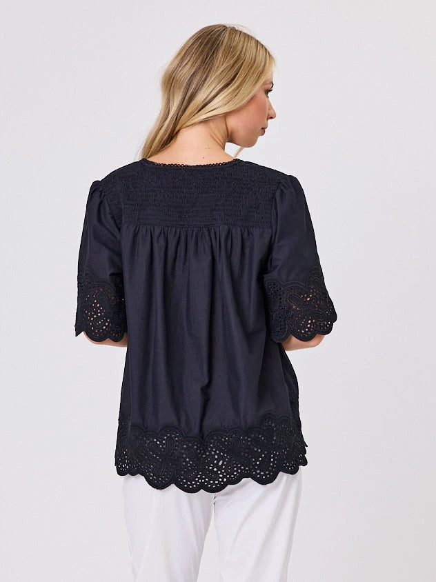 Woman wearing a black blouse with lace details standing front-on in studio light with white background. Top by Navy & Co nz fashion brand  