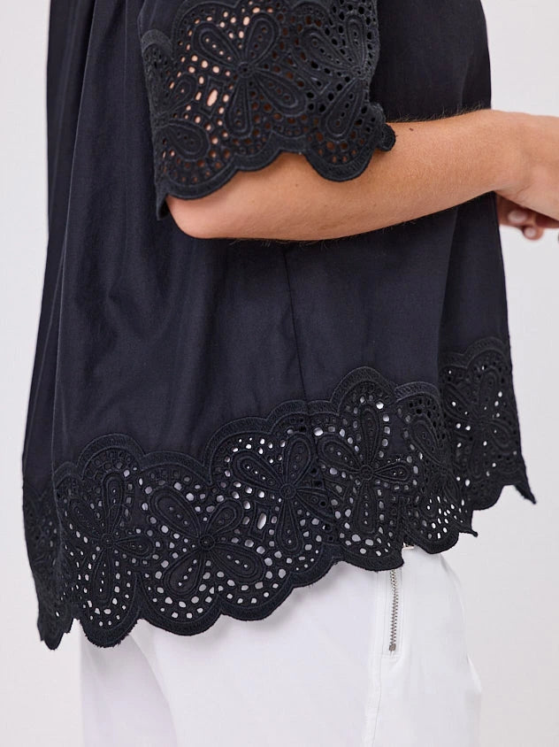 Woman wearing a black blouse with lace details standing front-on in studio light with white background. Top by Navy & Co nz fashion brand  