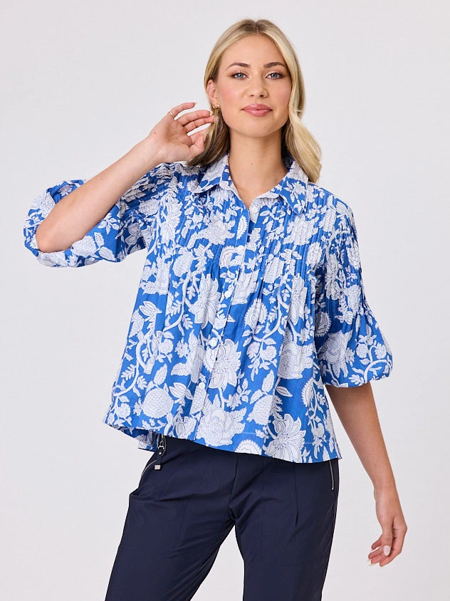 One woman dressed in blue tapestry cotton shirt, with bubble sleeves by Navy & Co a NZ fashion brand, she is standing front-on in studio light