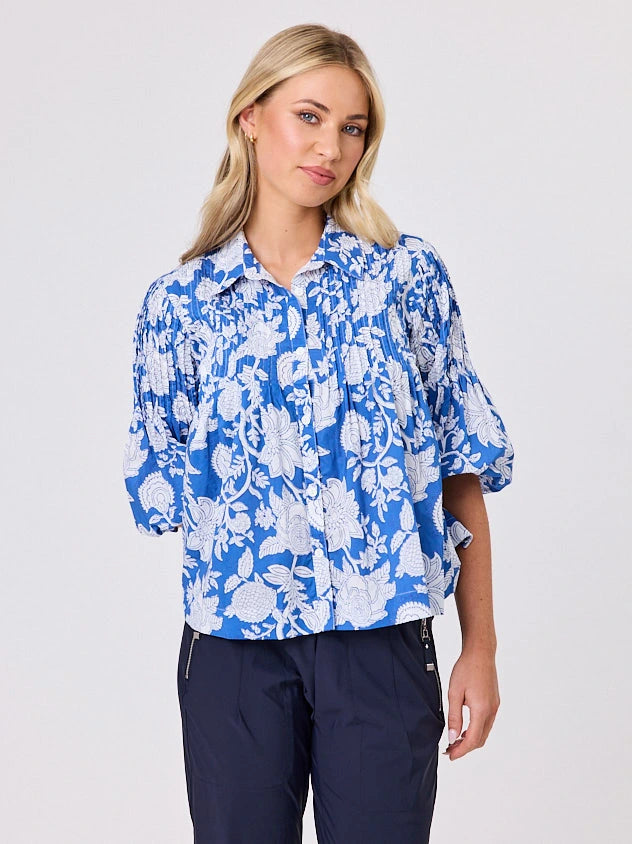 One woman dressed in blue tapestry cotton shirt, with bubble sleeves by Navy & Co a NZ fashion brand, she is standing front-on in studio light