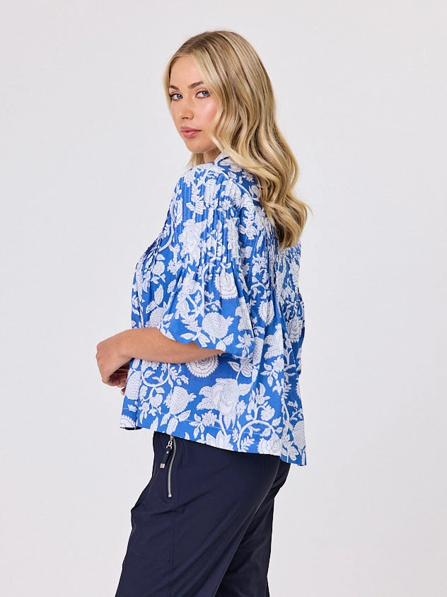 Woman wearing a blue floral blouse and navy an co pants on a white fashion studio background
