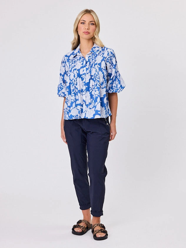 One woman dressed in blue tapestry cotton shirt, with bubble sleeves by Navy & Co a NZ fashion brand, she is standing front-on in studio light