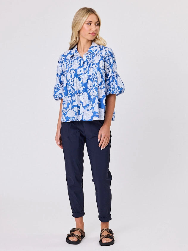One woman dressed in blue tapestry cotton shirt, with bubble sleeves by Navy & Co a NZ fashion brand, she is standing front-on in studio light