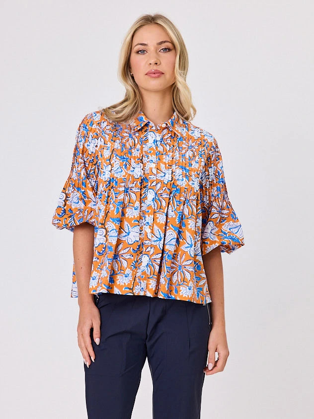 One woman dressed in orange tapestry cotton shirt, with bubble sleeves, by Navy & Co a NZ fashion brand, she is standing front-on in studio light