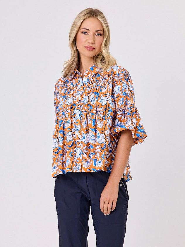 One woman dressed in orange tapestry cotton shirt, with bubble sleeves, by Navy & Co a NZ fashion brand, she is standing front-on in studio light