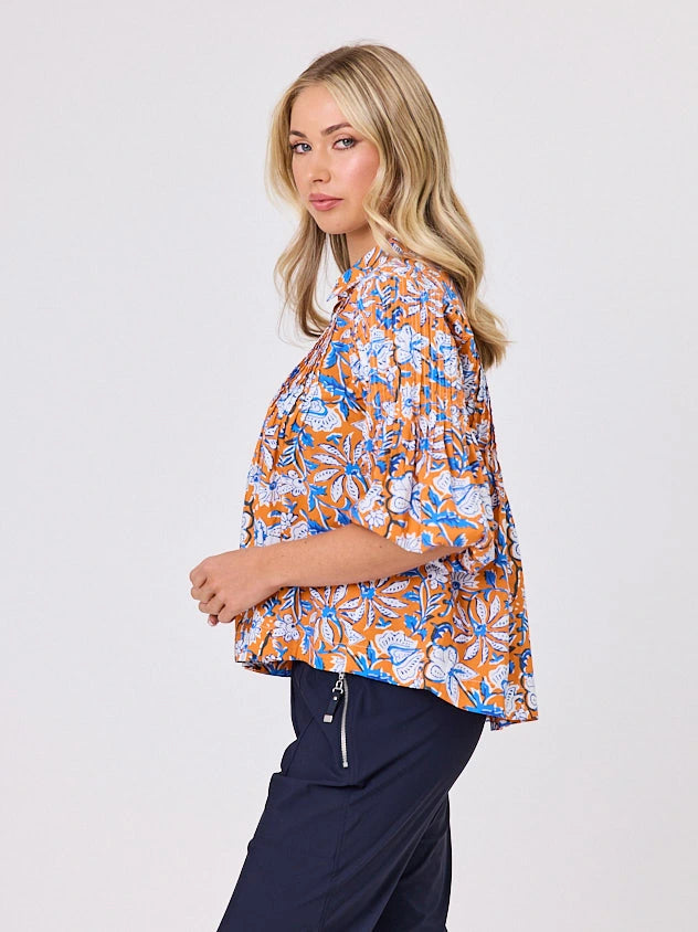 One woman dressed in orange tapestry cotton shirt, with bubble sleeves, by Navy & Co a NZ fashion brand, she is standing front-on in studio light