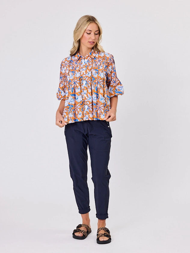 One woman dressed in orange tapestry cotton shirt, with bubble sleeves, by Navy & Co a NZ fashion brand, she is standing front-on in studio light