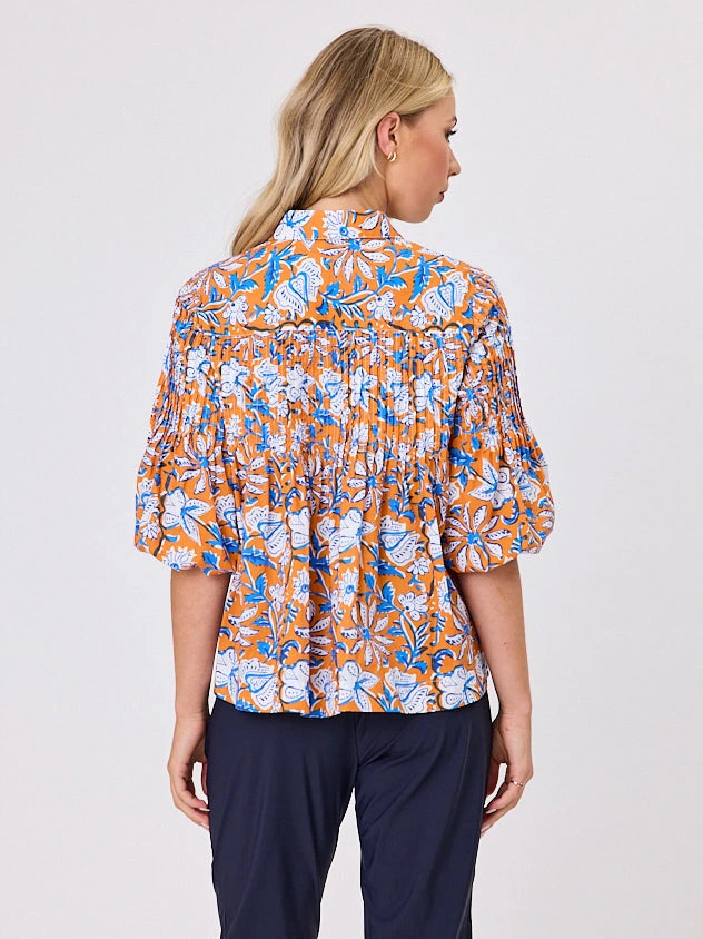 One woman dressed in orange tapestry cotton shirt, with bubble sleeves, by Navy & Co a NZ fashion brand, she is standing front-on in studio light