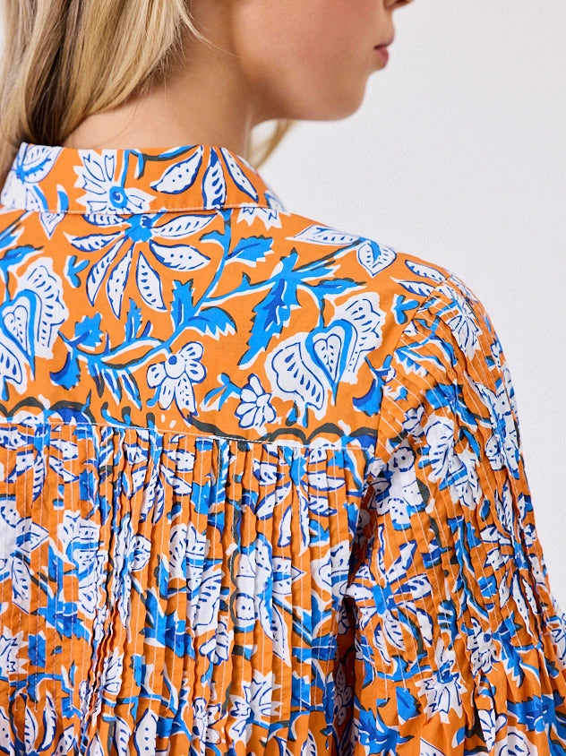 One woman dressed in orange tapestry cotton shirt, with bubble sleeves, by Navy & Co a NZ fashion brand, she is standing front-on in studio light